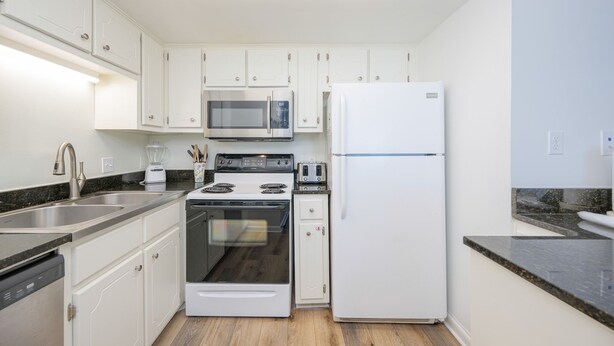 A modern kitchen with white cabinets, a stainless steel sink, a microwave, a stove, and a refrigerator. - Island Winds East 309 2 Bedroom Condo (Gulf Shores)