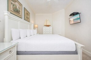 A neatly arranged bedroom with a bed, bedside tables, a lamp, and a wall-mounted TV. - The Oasis 706 Formerly Phoenix West Ii 706 3 Bedroom Condo (Orange Beach)