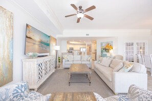 A spacious living room with a large flat-screen TV, a ceiling fan, and a view into the kitchen. - The Oasis 706 Formerly Phoenix West Ii 706 3 Bedroom Condo (Orange Beach)