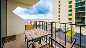 A balcony with a table and chairs, overlooking a parking area and a building with multiple balconies. - Island Winds East 210 2 Bedroom Condo (Gulf Shores)