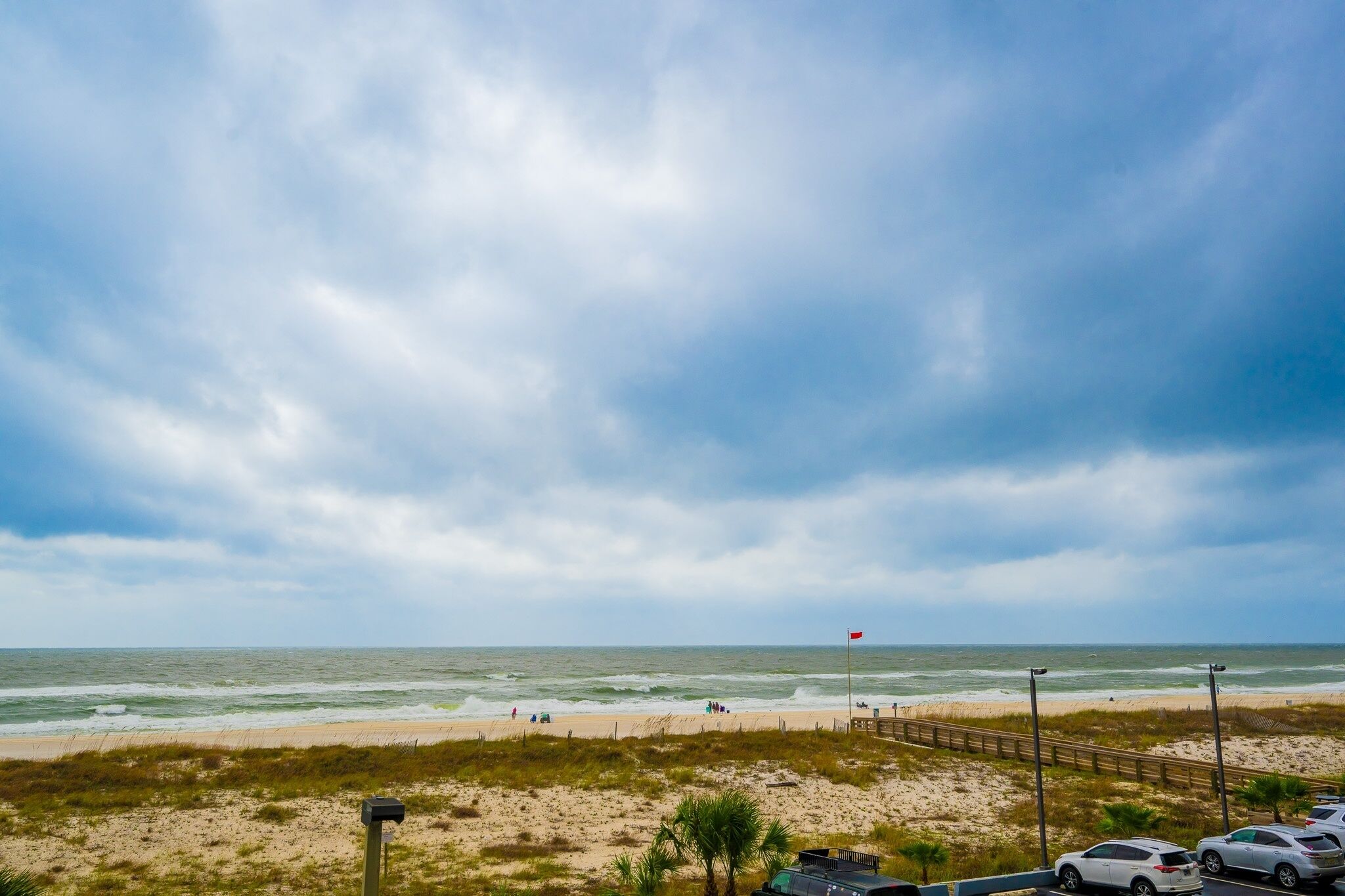 A beach with a sandy shore, a wooden boardwalk, and a flagpole with a flag.