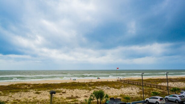 A beach with a sandy shore, a wooden boardwalk, and a flagpole with a flag. - Island Winds East 210 2 Bedroom Condo (Gulf Shores)
