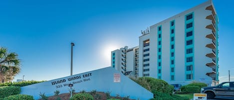 Un hotel de varios pisos llamado 'Island Winds East' en el número 333 de West Beach Blvd., con un letrero de estacionamiento privado y un aviso de seguridad.