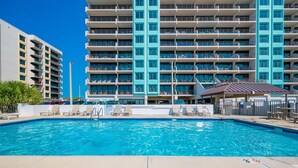 A swimming pool with lounge chairs and a building with multiple balconies in the background. - Island Winds East 307 2 Bedroom Condo (Gulf Shores)