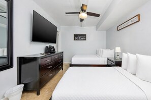 Une chambre d’hôtel comprenant un lit, une télévision, un ventilateur de plafond, une table de chevet avec une lampe et un panneau mural.