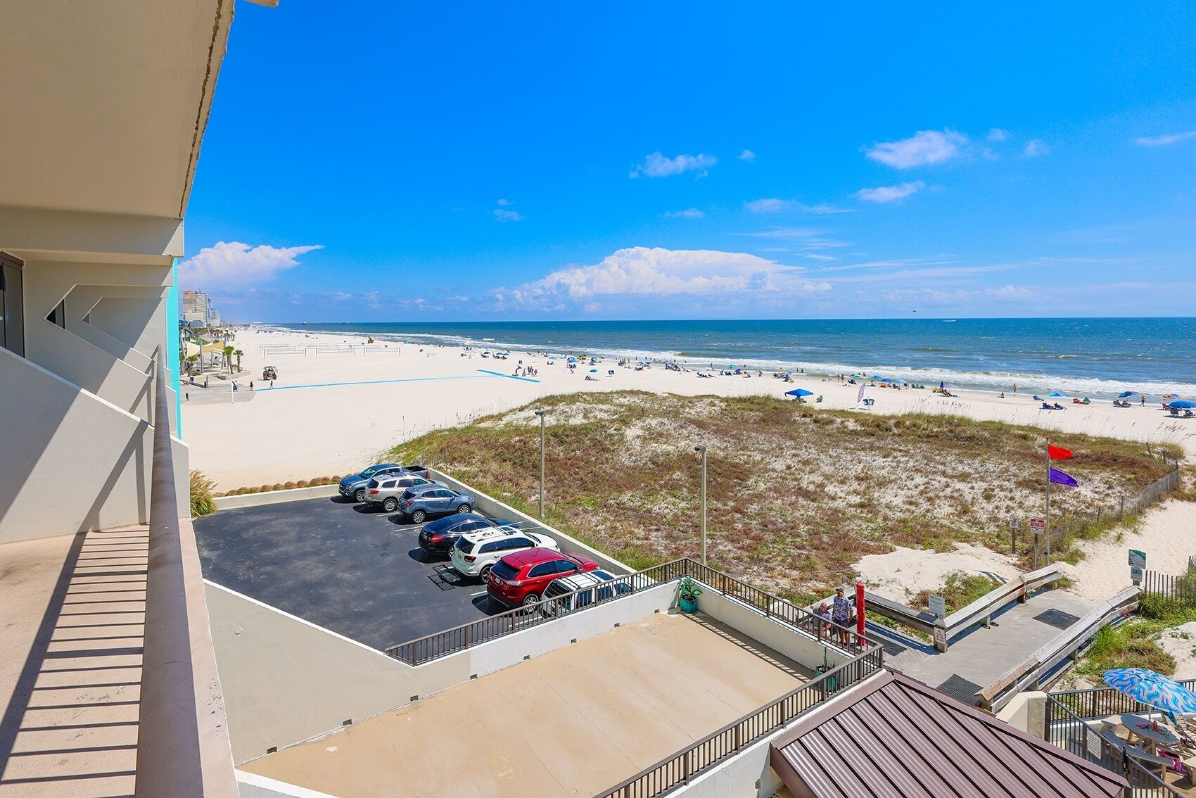 A beachfront hotel with a parking lot, beach view, and a boardwalk with umbrellas.