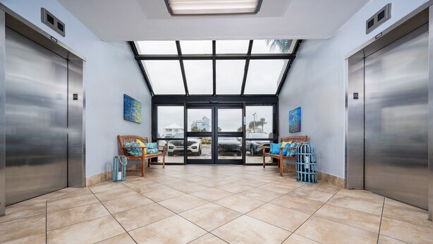 A hotel lobby with two elevators, a large glass door entrance, and a tiled floor. - Island Winds East 702 2 Bedroom Condo (Gulf Shores)