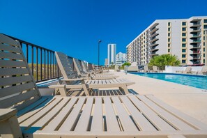 Uma área à beira da piscina com espreguiçadeiras e uma piscina, rodeada por edifícios altos.