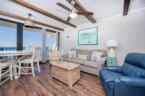 A spacious balcony with a dining table and chairs, a sofa, a blue leather chair, and a wooden coffee table. - Island Winds East 708 2 Bedroom Condo (Gulf Shores)