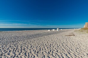 Ein weiter Sandstrand mit Fußspuren, die zum Wasser führen, ein klarer blauer Himmel und einige Personen in der Ferne.