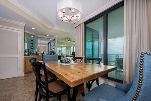 Un vaste espace dédié à la salle à manger, avec une table et des chaises en bois, un lustre et une vue sur le balcon grâce à de grandes fenêtres.