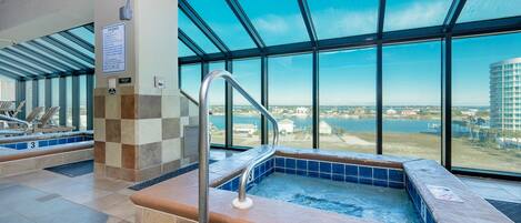 A hot tub area with a view of a body of water and buildings, a tiled floor, and a metal handrail.