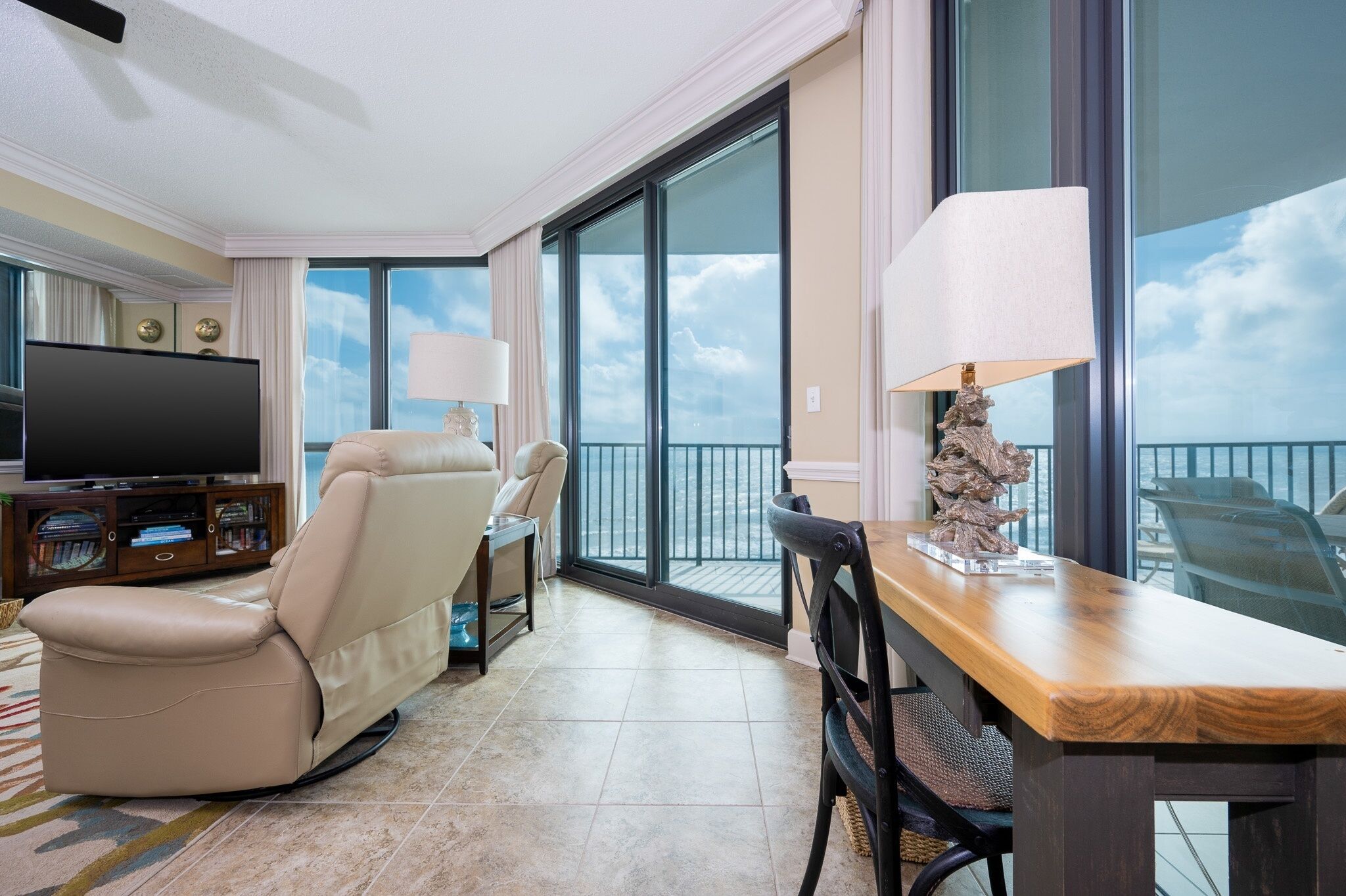 A spacious living area with a flat-screen TV, leather recliner, and a dining table with a lamp.