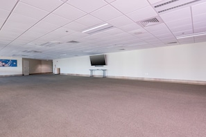 A large, empty room with a carpeted floor, white walls, and a flat-screen TV mounted on the wall. - Phoenix Ix 1002 2 Bedroom Condo (Orange Beach)