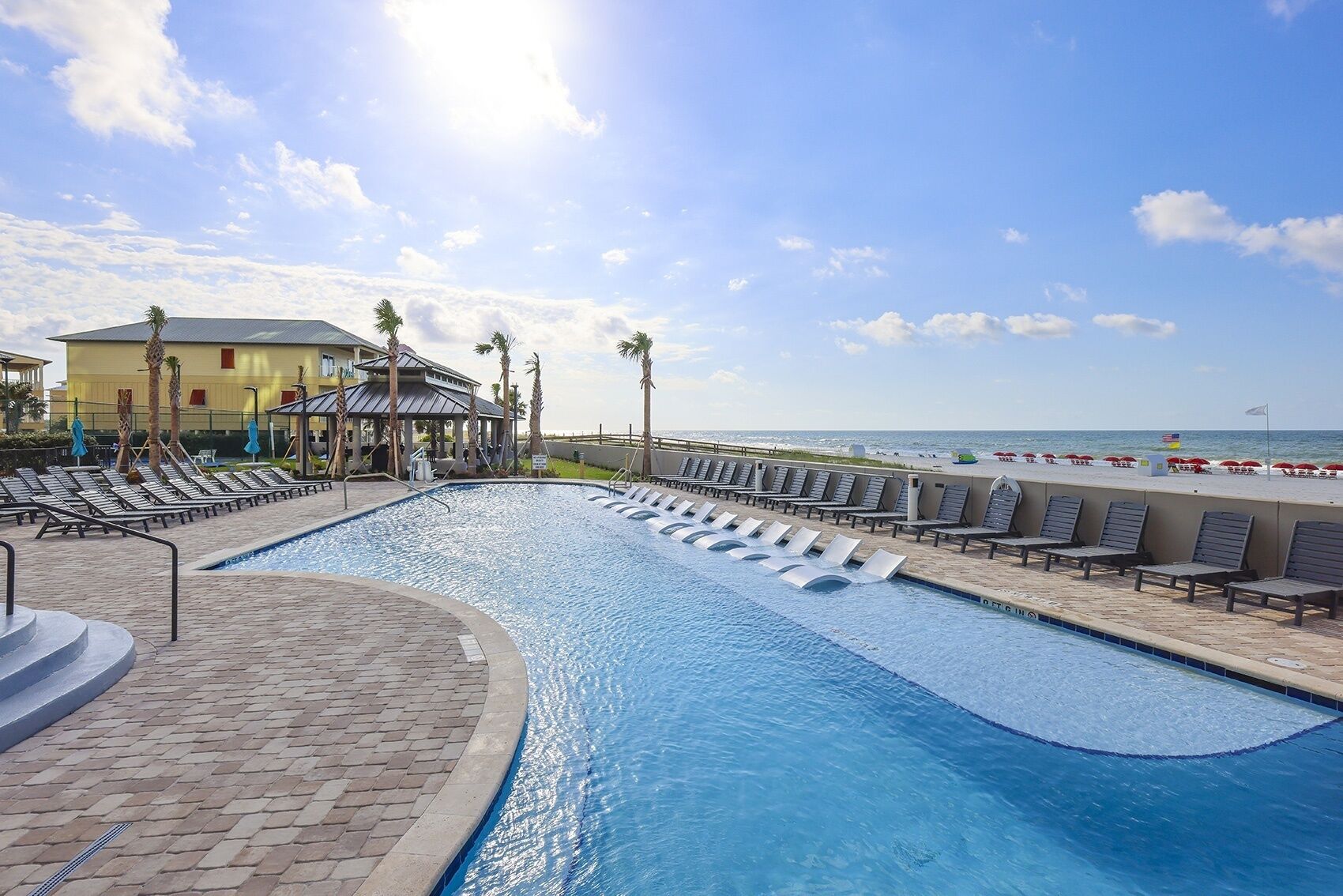 A swimming pool with lounge chairs and a beach view.