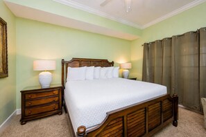 Uma cama bem arrumada com cabeceira de madeira, duas mesas de cabeceira com abajures e uma janela grande com cortinas.