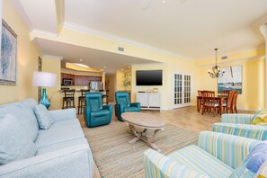 Uma sala de estar ampla com sofá, cadeiras, mesa de centro e um espaço de jantar com cadeiras e mesa.