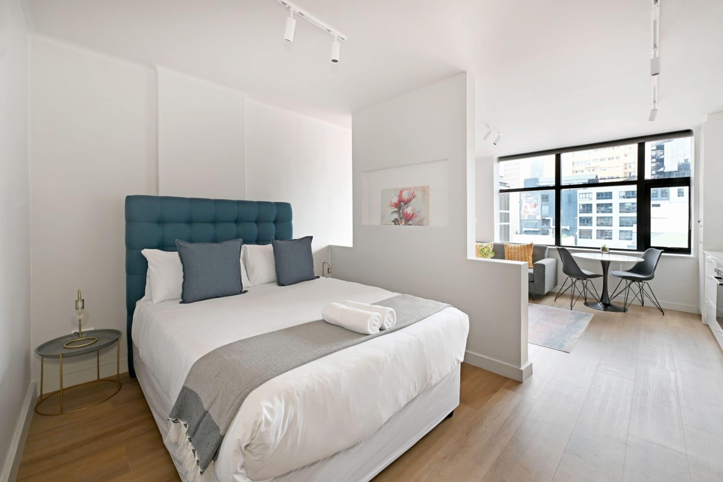 A modern bedroom with a large bed, a desk, and a view of the city through large windows.