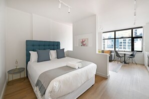 Ein modernes Schlafzimmer mit einem großen Bett, einem Schreibtisch und Blick auf die Stadt durch große Fenster.