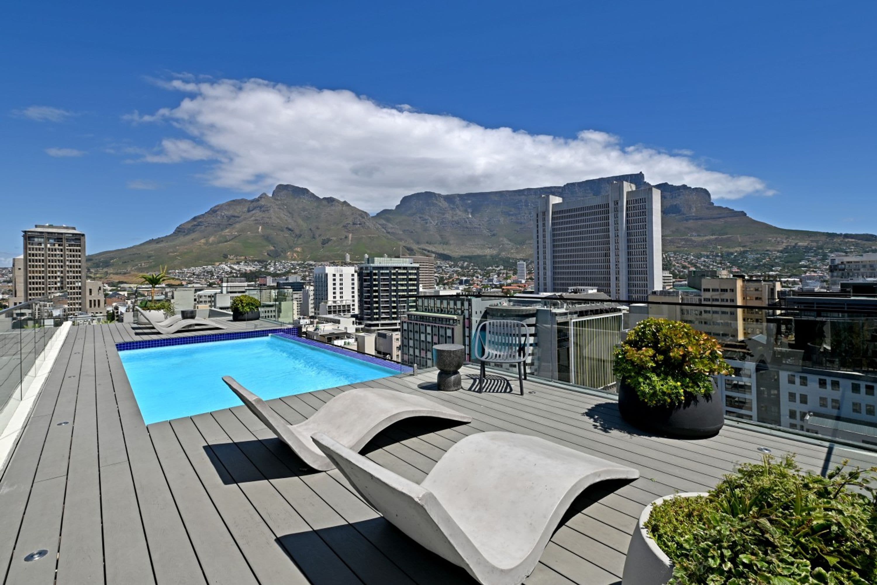 A rooftop pool with lounge chairs and a view of a cityscape and mountains.