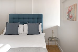 Ein Schlafzimmer mit einem Bett, Kissen, einem Nachttisch und einem an der Wand befestigten Kunstwerk.