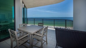 A balcony with a table and chairs, a view of the ocean, and a beach in the background. - Phoenix Ix 902 2 Bedroom Condo (Orange Beach)