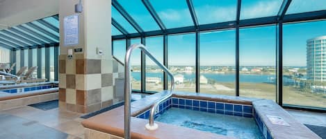 A hot tub area with a view of a body of water and buildings, a tiled floor, and a metal handrail.