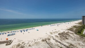 A beach with a clear sky, a sandy shore, and a building in the background. - Phoenix Ix 902 2 Bedroom Condo (Orange Beach)