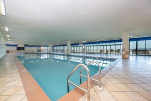 Ein beheiztes Hallenbad mit klarem, blauem Wasser, Fliesenboden und einer Metallleiter.