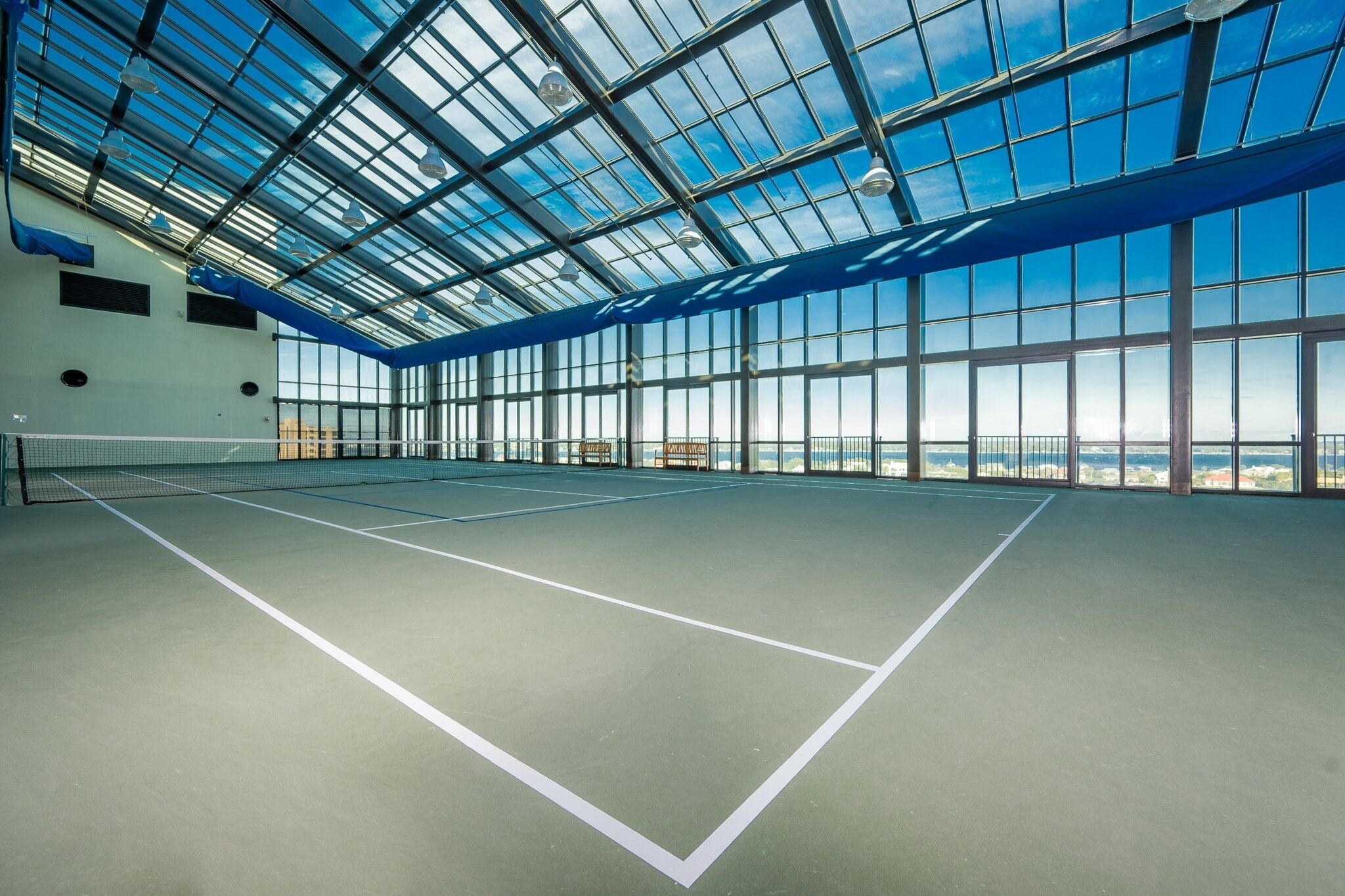 Una cancha de tenis interior con techo de vidrio y vistas a la ciudad.