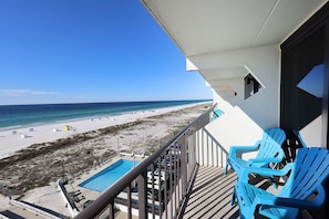 A balcony with a pool and beach view, blue chairs, and a clear sky. - Island Winds East 503 2 Bedroom Condo (Gulf Shores)