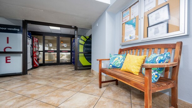 A lobby with a wooden bench, tiled floor, vending machines, and a wall with informational posters. - Island Winds East 503 2 Bedroom Condo (Gulf Shores)