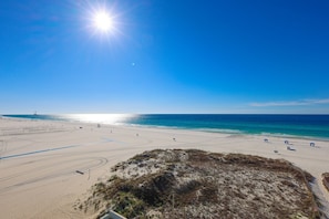 A beach with clear skies, a sandy shore, and a few umbrellas. - Island Winds East 503 2 Bedroom Condo (Gulf Shores)