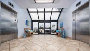 A hotel lobby with two elevators, a large glass door entrance, and a tiled floor. - Island Winds East 503 2 Bedroom Condo (Gulf Shores)