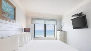 A hotel room with a bed, a television, a window with a view of the sea, and a painting on the wall. - Island Winds East 503 2 Bedroom Condo (Gulf Shores)