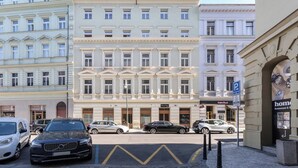 Ein mehrstöckiges Hotel mit klassischer Architektur, das einen zentralen Eingangsbereich mit einer imposanten Treppe und einen Parkplatz davor zeigt.