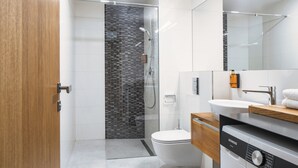 Ein modernes Badezimmer mit Duschkabine aus Glas, Toilette, Waschbecken und Waschmaschine.