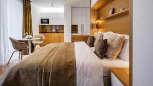 Ein Hotelzimmer mit Bett, Nachttisch, Schreibtisch mit Stuhl, einer Küchenzeile und einem Fernseher.