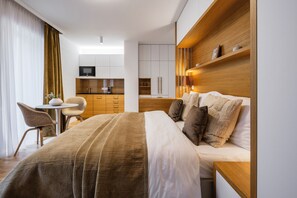 A hotel room with a bed, bedside table, a desk with a chair, a kitchenette, and a TV. - My Second Home - Soukenická 36 Residence (Hlavní město Praha)