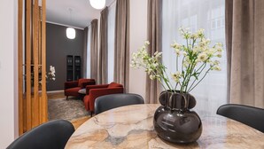 Ein modernes Hotelzimmer mit einem Marmoresszimmer, roten Sofas, einer Blumenvase und Blick auf die Stadt durch große Fenster.