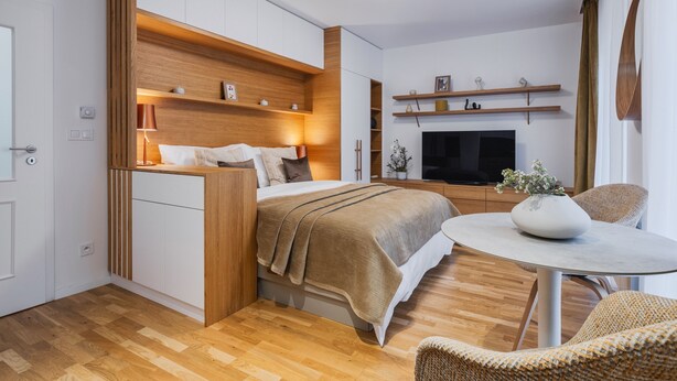 Ein modernes Schlafzimmer mit Bett, Nachttischen, Fernseher, kleinem Esstisch und Stuhl.