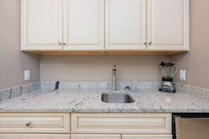 A kitchen with white cabinets, a granite countertop, a stainless steel sink, and a blender. - The Oasis 1409 Formerly Phoenix West Ii 1409 3 Bedroom Condo (Orange Beach)