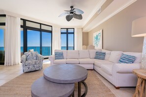 A spacious living room with a large sectional sofa, a round coffee table, and a patterned armchair. - The Oasis 1409 Formerly Phoenix West Ii 1409 3 Bedroom Condo (Orange Beach)