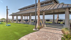 A covered outdoor area with a brick pathway, palm trees, and a view of the ocean. - The Oasis 1409 Formerly Phoenix West Ii 1409 3 Bedroom Condo (Orange Beach)