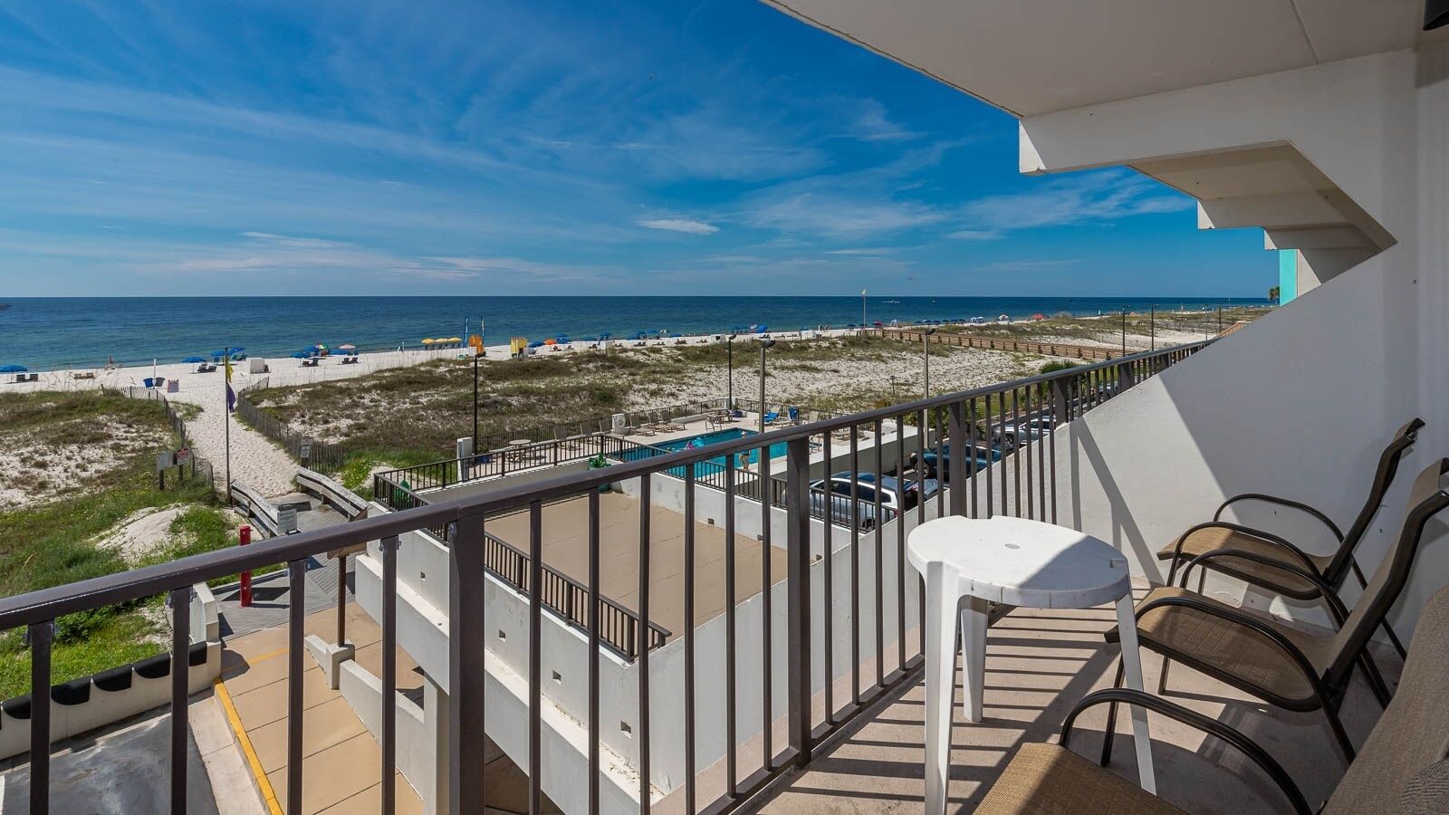 A balcony with a view of the beach and ocean, a pool, and outdoor seating.