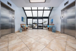 A hotel lobby with two elevators, a large glass door entrance, and a tiled floor. - Island Winds East 604 1 Bedroom Condo (Gulf Shores)