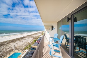 Ein Balkon mit Blick auf Strand und Meer, ein Schwimmbad und blaue Stühle.