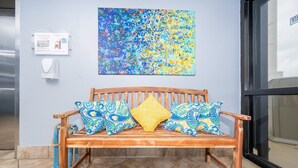 Um banco de madeira com almofadas estampadas em frente a uma parede com uma pintura abstrata colorida.