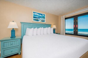 Une chambre d’hôtel avec un lit, deux tables de chevet, un tableau et une vue sur l’océan.