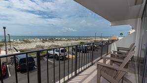 A balcony with a view of a beach and parked cars. - Island Winds East 109 2 Bedroom Condo (Gulf Shores)